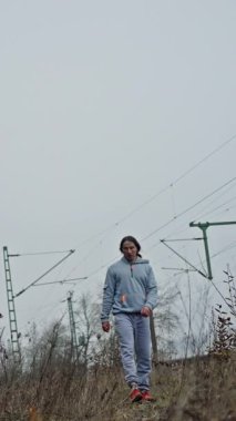 Kapüşonlu adam otlakta dolaşıyor. Gri Kapüşonlu Adam Direkler Arasında Sabit Yürüyor. Beyaz erkek kapüşonlu ve kırmızı pabuçlu. Tepesinde sütunlar var.