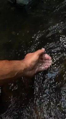 El Cupping Stream Nehir yatağı, Açık Hava Yürüyüşçüsü Akıntıyı ve Susuzluğu Denemek için Duraksıyor, El ve Bileklerin Dokunsal Kapanışı Çakıl Taşları Üzerinde Parıldıyor, Nazik Akış ve Meditasyon İçin Sakin Oku