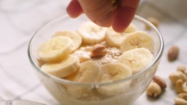 Bir gecelik yulaf ezmesi kasesi. Evde sağlıklı kahvaltı hazırlıyorum. Bitki sütü dökülüyor. Muz, bal ve fındık malzemeleri. 4K video. Adım adım tarif