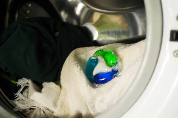 Gel caps lay in washing machine with dirty clothes. Household laundry equipment. Spring cleaning.