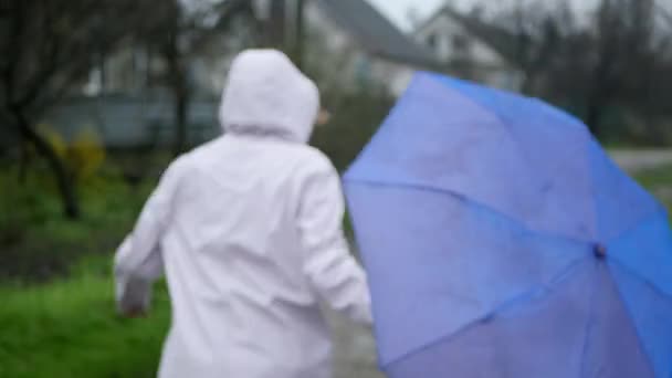 雨の下で楽しみを持っている傘とレインコートやゴムブーツの女性 — ストック動画