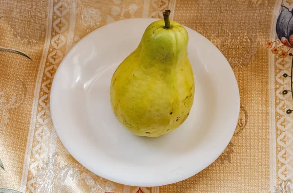 花の生地の上に白い板に立つことは 茎を持つ孤立した黄色の熟した洋ナシ形のグアハヴァです — ストック写真