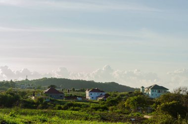 Mavi gökyüzü ve evlerle benekli yeşil manzara sabah güneşiyle ışıldıyor..