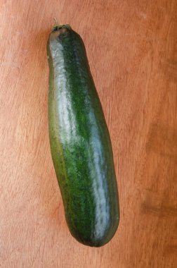 Kapalı alanda, doğal kahverengi bir levha yüzeyinde uzun yeşil bir kabak kabağı bulunur.