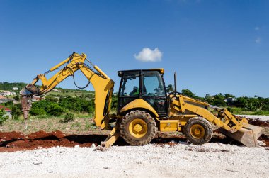 Sarı bir buldozer, kepçe koluna bağlı bir kaya matkabı ile Jamaika 'da bir yol inşaatının siperine demirlemiş ve siperin kaya içeriğini parçalamaya başlamak üzere..