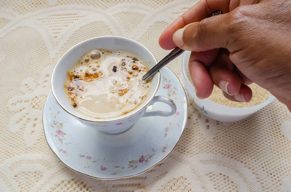 Sıcak sütlü kahve içeceği ile dolu bir çay fincanına yerleştirilmiş çay kaşığının sapını tutuyorum..