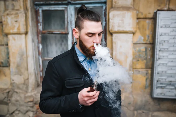 Чоловік з бородою курить електронну сигарету на відкритому повітрі — стокове фото