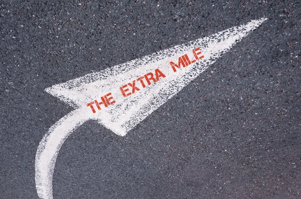 Flèche dirigée peinte en blanc avec des mots THE EXTRA MILE sur la surface de la route — Photo