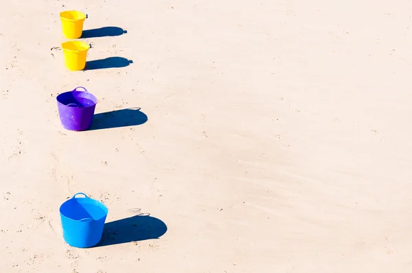 Row of colorful buckets on the beach sand — Stock Photo, Image