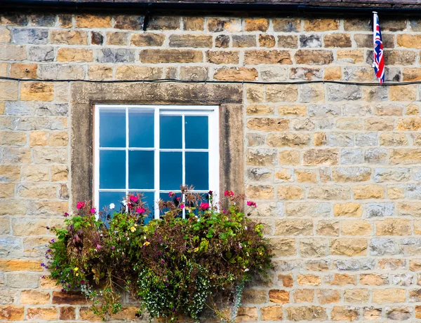 Architecture detail of traditional English cottage, with pots of flowers at the window and British flag on the wall — Stock Photo, Image