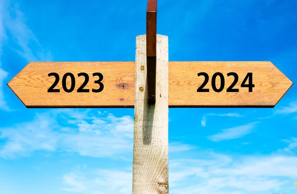 Wooden signpost with two opposite arrows over clear blue sky, year 2023 and 2024 signs, Happy New Year conceptual image — Stock Photo, Image