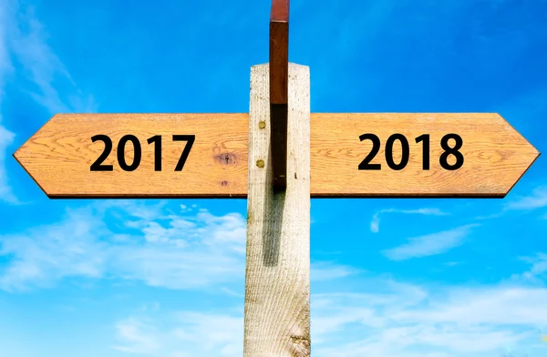 Placa de madeira com duas setas opostas sobre céu azul claro, ano 2017 e 2018 sinais, imagem conceitual Feliz Ano Novo — Fotografia de Stock