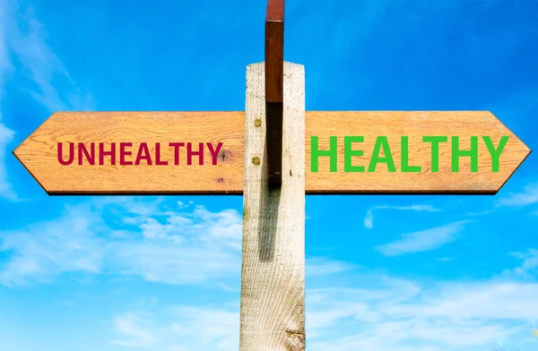 Papan nama kayu dengan dua panah berlawanan di atas langit biru yang jernih, pesan sehat versus tidak sehat, gambar konseptual gaya hidup yang sehat — Stok Foto
