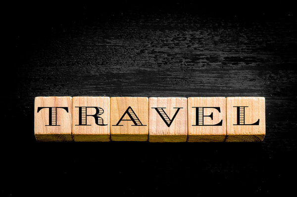 Word Travel. Wooden small cubes with letters isolated on black background.Concept image.