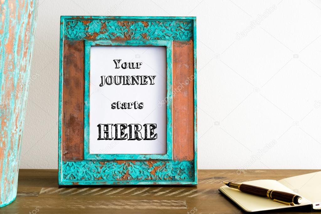 Vintage photo frame on wooden table with text YOUR JOURNEY STARTS HERE