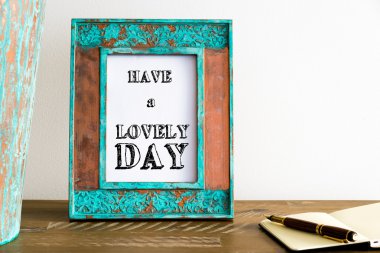Vintage photo frame on wooden table with text HAVE A LOVELY DAY