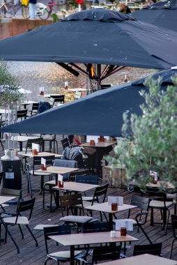 Açık teras, siyah şemsiyeler, boş masalar ve Hollanda, Leiden 'da deniz kenarında sandalyeler, sıcak nehir kenarı yemek düzeneği ve akşam misafirleri için ısıtıcılar hazır.