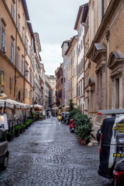 19 Ocak 2026, Roma, İtalya, Narrow kaldırım taşı caddesi tarihi binalar, kafeler ve park halindeki scooterlarla dolu bulutlu bir günde Roma 'nın orta kesiminde yerel halk ve ziyaretçiler arasında popüler oldu.