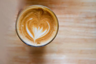 Latte sanat kahvesi ve cam bardak ahşap masada.