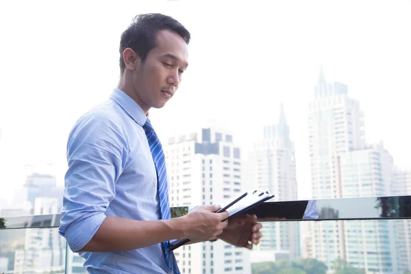 Smart Asian Business man using smart phone and document to working on window with city building and green balcony