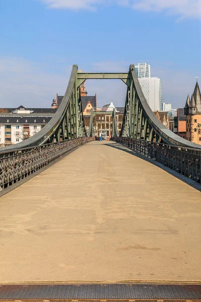 Direct view of the historic pedestrian bridge over the Main in Frankfurt. Houses of the old town in the background with sunshine and a few clouds. Bridge with iron terrain