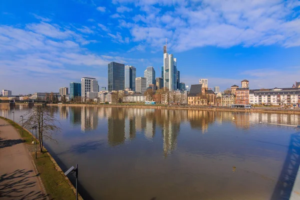 Financial district with skyscraper of Frankfurt am Main. River with reflections in the foreground on a sunny day. Bank on the river in spring