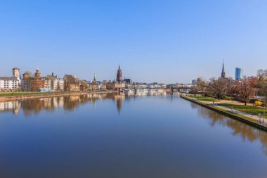 Nehir kenarındaki Panorama Frankfurt 'ta. Ana caddenin kıyısına park et. Ağaçlar, çimenler, güneş ışığı ve mavi gökyüzü. Frankfurt Katedrali ve demir köprüsü olan eski kasabanın binaları