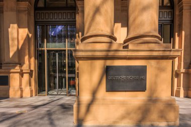 Girişinde Alman borsası binasının kahverengi cephesi olan beton bir taban. Metal panelli güneş ışığında tarihi bir ev. Arka planda cam kapılar.