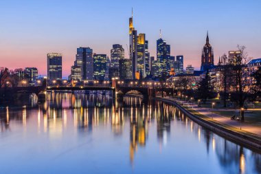Gün batımından sonra Frankfurt şehri ufuk çizgisi. Yüksek binaların iş ve finans merkezlerinden aydınlatılmış binaları. Nehir üzerindeki köprü Sokak ışıklarıyla