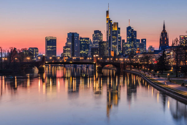 Frankfurt skyline in the evening at sunset. High-rise buildings from the financial district and river Main with reflections. Illuminated houses and bridge