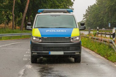 Otobanda bir polis arabası var. Brandenburg eyaletinden bir aracın park yerinde ön görüntüsü. Acil bir durağın asfalt yolu. Arka planda yol işaretleri olan ağaçlar ve çarpışma engelleri
