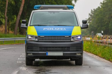 Otobanda ışıkları açık bir polis arabasının önü. Brandenburg eyaletinden bir araç bir otoparkta. Acil bir durum için asfalt yol. Korumalar ve ağaçlar ile duracağız.