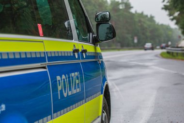 Arka planda otoyol olan bir Alman polis aracının yan görüntüsü. Polis arabası mavi ve sarı renkte. Asfalt yolu olan acil servis. Arka planda ağaçlar ve korkuluklar