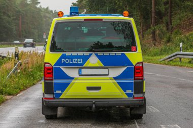 Brandenburg otobanından gelen bir devriye aracının arka görüntüsü. Islak yolda sarı ve mavi boyalı polis arabası. Mavi ışık ve polis kapısında yazı var.