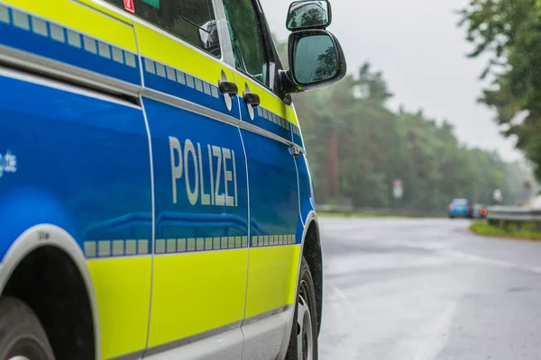 ドイツの警察車両の助手席側 外装ミラーで体の上のレタリング警察のビュー 反射ストライプと青の背景と黄色の色 雨天時のアスファルト道路 — ストック写真
