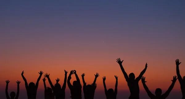 Pessoas silhuetas com as mãos levantadas desfrutando de um gradiente de nascer do sol — Fotografia de Stock