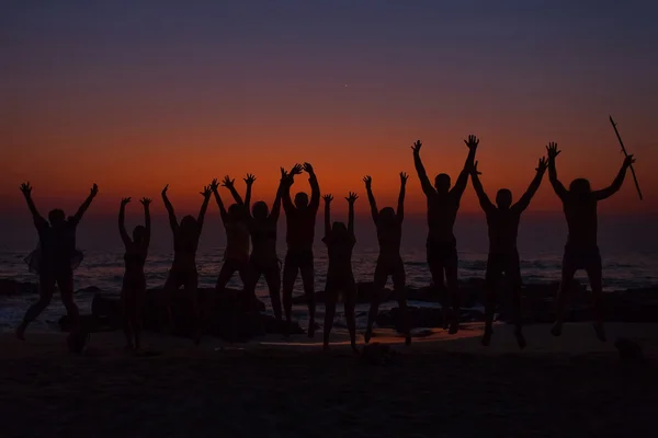 Pessoas silhuetas com as mãos levantadas na areia goa cada um com sunri — Fotografia de Stock