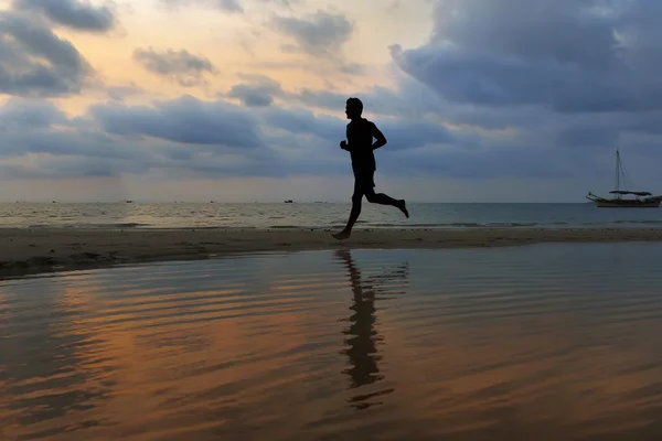 Atleta corre ao longo da praia de areia com espelho na água e o — Fotografia de Stock