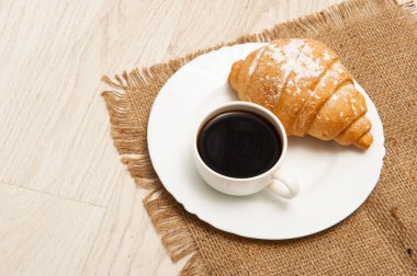 Bir fincan çay tabağında kruvasan ve bir fincan kahve. Üst görünüm