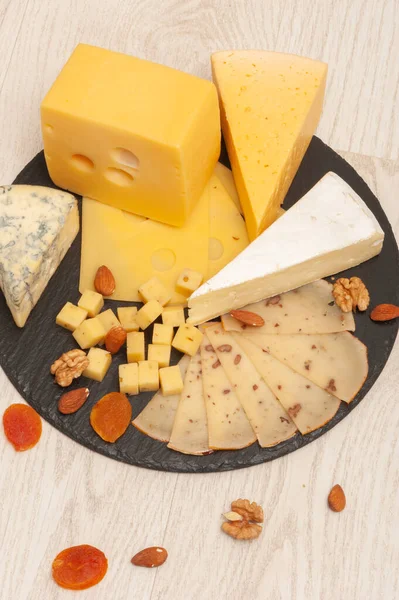 Diferentes tipos de queso en una tabla de grafito negro con albaricoques secos, nueces. Vista superior —  Fotos de Stock