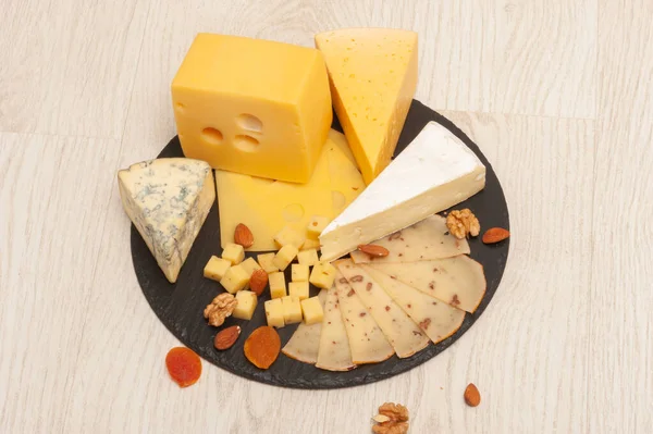 Diferentes tipos de queso en una tabla de grafito negro con albaricoques secos, nueces. Vista superior —  Fotos de Stock