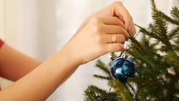 Uma jovem decora uma árvore de Natal com bolas azuis. — Vídeo de Stock