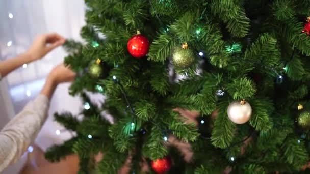 En ung kvinna dekorerar med julbollar en fluffig julgran i rummet. Vacker ljus jul bakgrund. Festlig julstämning. — Stockvideo