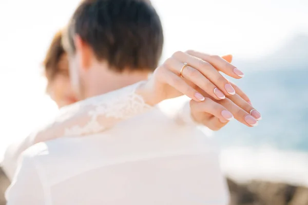 Novia y novio se abrazan en la playa rocosa de la isla Mamula, la novia puso sus manos sobre los hombros de los novios — Foto de Stock