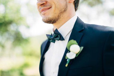 Damat papyon ve yaka çiçeğiyle düğün elbisesi içinde gülümsüyor.