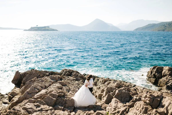 Novia y novio se abrazan en la playa rocosa de la isla Mamula cerca de la fortaleza de Arza — Foto de Stock