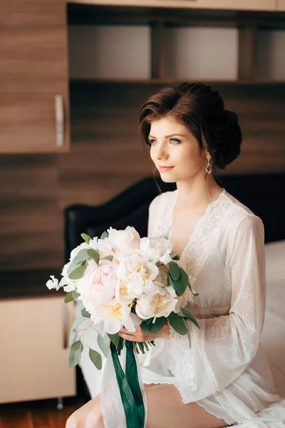 Bella sposa tenera con bouquet da sposa di rose crema ed eucalipto seduto sul letto in una camera d'albergo — Foto Stock