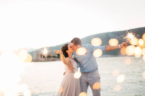 La mariée et le marié s'embrassant sur la plage de l'île de Mamula et tenant des étincelles — Photo