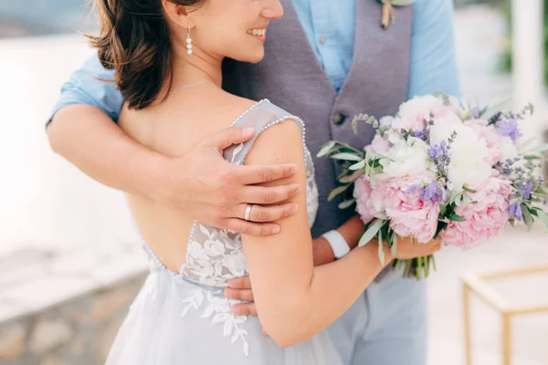 El novio abraza suavemente a la novia por detrás de la novia tiene un ramo en sus manos — Foto de Stock