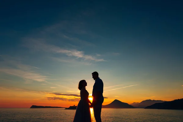 La novia y el novio de pie en la playa de la isla de Mamula y tomados de la mano al atardecer — Foto de Stock
